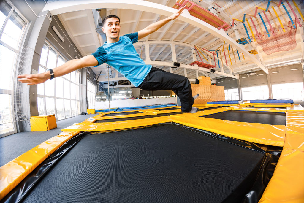 Happy emotional man jumping and flying in trampoline sport center indoors